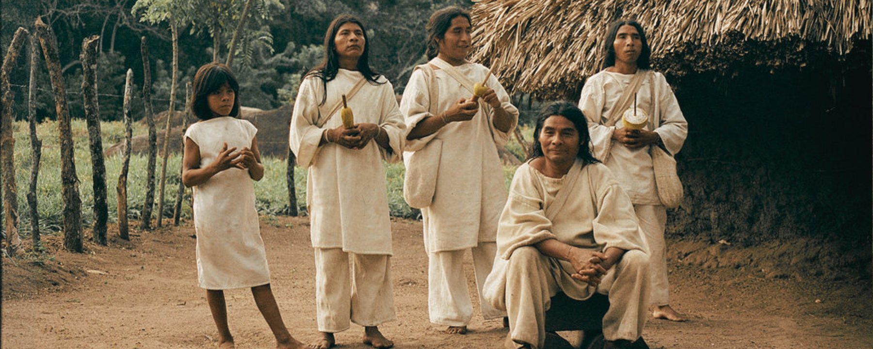 Kággaba women, a child and a man in white cotton clothing in front of a thatched house